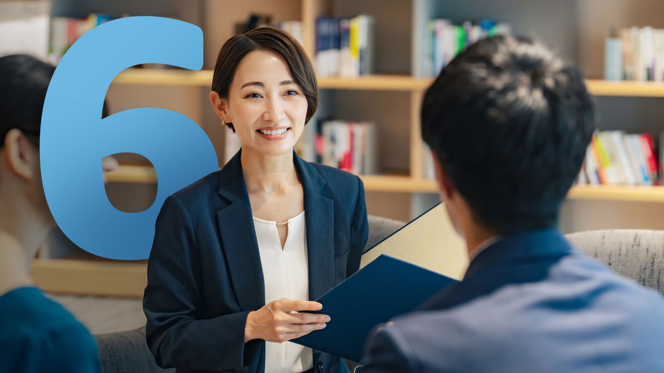 スーツ姿の笑顔の女性が顧客と話している　その背景に水色で６の文字