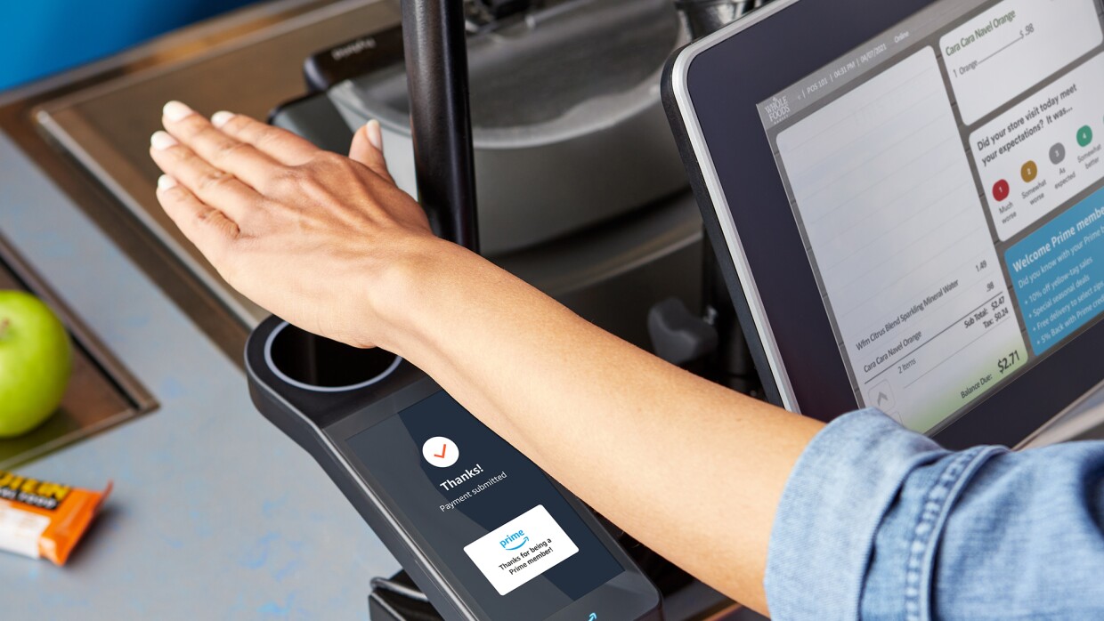 A hand hovers over a scanner at a grocery store, allowing a woman to check out and purchase her items.