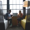 Man taking notes as his female colleague works on a laptop, in a casual work space.