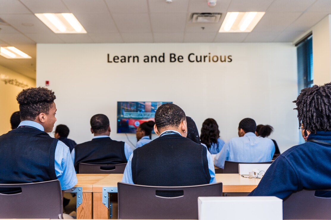 Shown from behind, students are seated at door desks in a classroom space within an Amazon fulfillment center in Etna, Ohio.