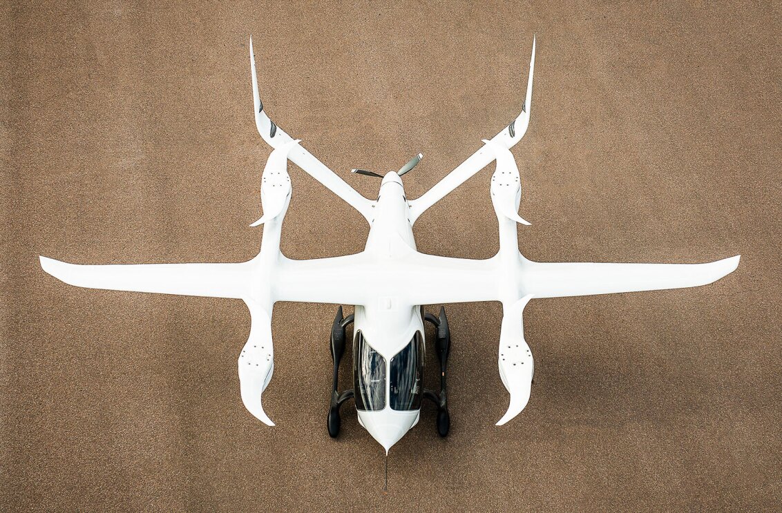 Overhead view of a small, aerodynamic, white aircraft with four small rotors on the top of the craft.