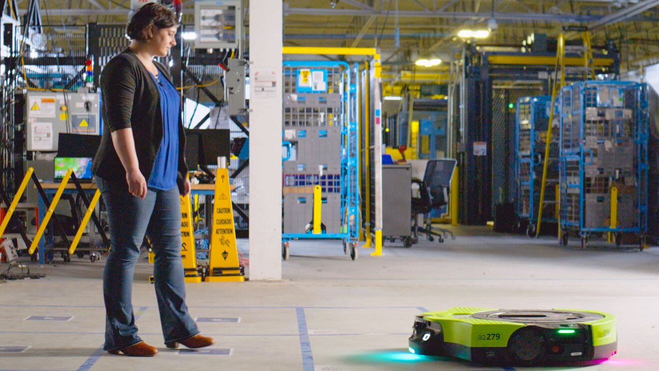 Woman looking down at a robot on the floor in an Amazon warehouse.