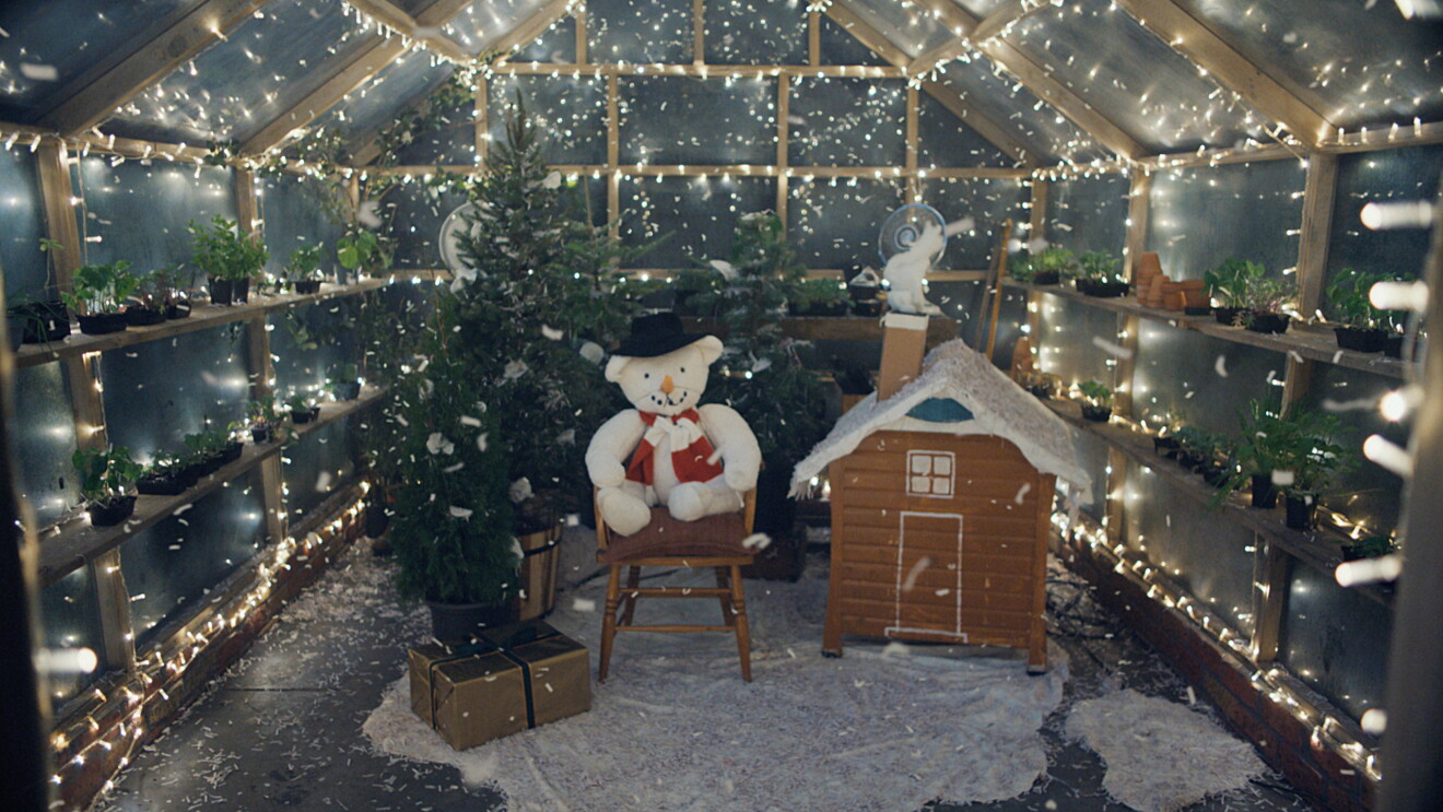 Del anuncio de Navidad de 2022, la foto está tomada desde dentro del invernadero que reproduce la bola de cristal de nieve. Las paredes transparentes tiene luces de Navidad y plantas. En el centro tres árboles de Navidad, un peluche que va vestido de muñeco de nieve y una casa hecha de cartón. Hay papeles que reproducen nieve en el suelo y volando por dentro del invernadero. 