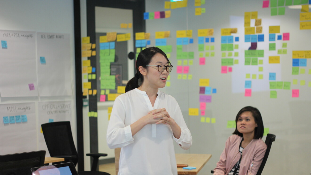 A lady in a white top presenting to a group brainstorm, planning setting