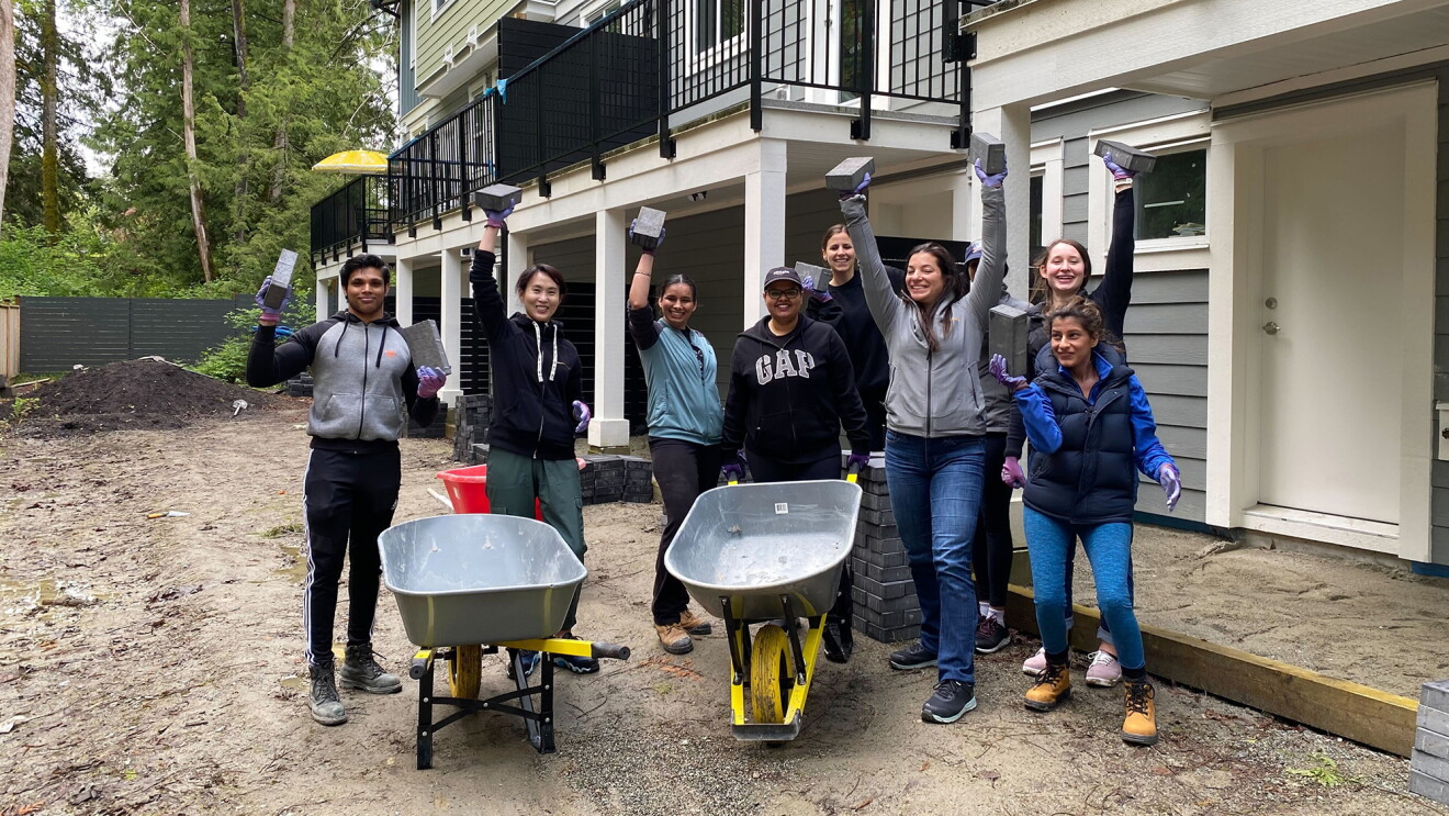 A photo of  ight employees standing behind two wheel burrows, in front of newly-built homes, participating in Amazon Habitat Build Days in Vancouver.