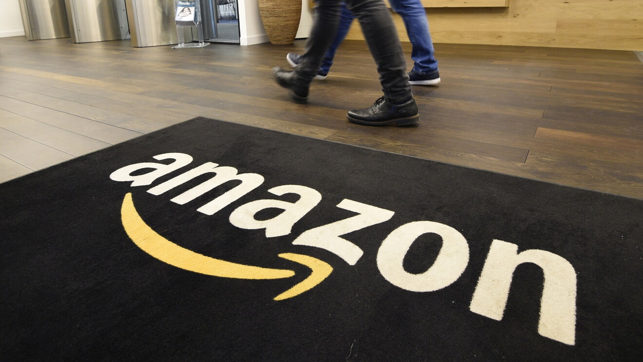 Amazon Development Centre Scotland mat with the amazon logo, two people are walking next to it. 
