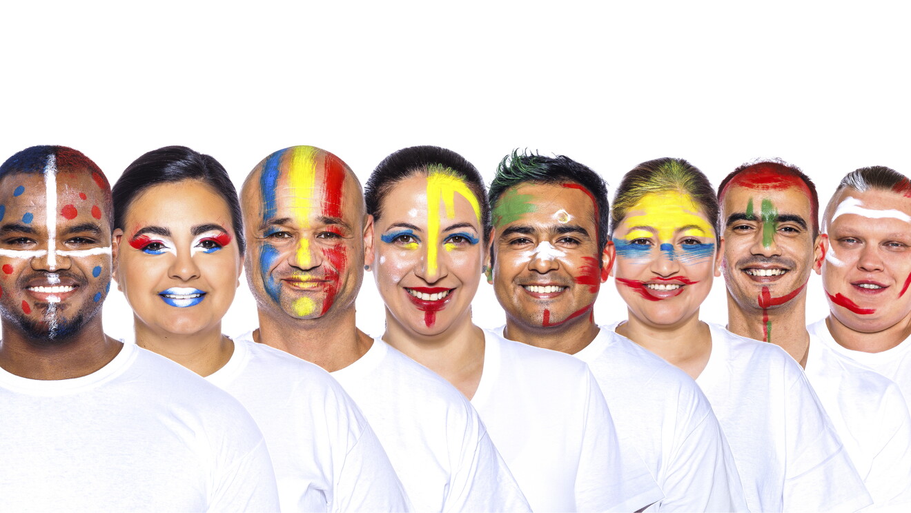 Para el Día de la diversida Amazon ha preparado una acción con asociados de diferentes países que llevan la bandera pitnada en su cara. En la foto, con camiseta blanca 8 trabajadores de Amazon con una camiseta blanca y mirando sonriendo a cámara.  Ángel, Ingrid, Adrián, Giselle, Ricardo, Gladys, Mohamed y David. 