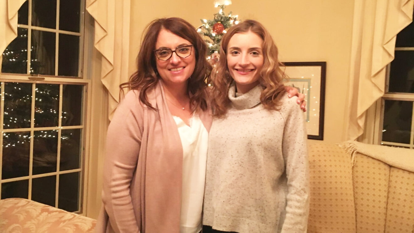 An image of two women smiling for a photo in front of a Christmas tree in their living room.