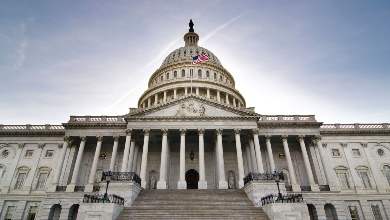 An image of the U.S. Capitol building with a flag on the top and blue skies behind it.