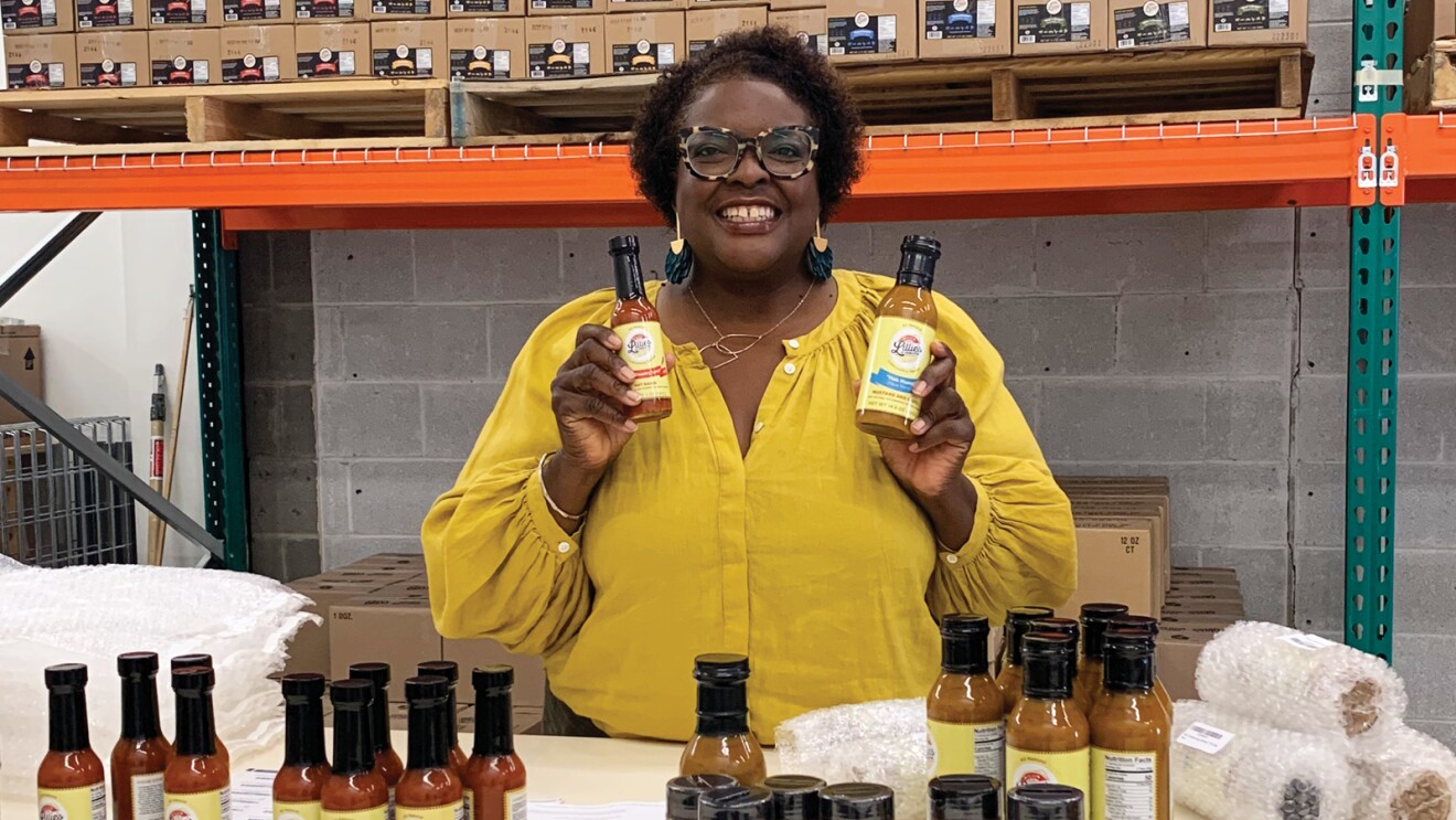 A photo of Tracey Richardson, CEO and co-founder of Lillie's of Charleston, holding two hot sauce products. 