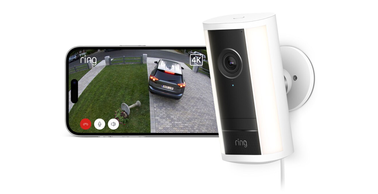 カメラの映像を表示する横長のディスプレイ、右側に白い円柱状筐体の監視カメラ。画面には石畳のアプローチと芝生の前庭が映っている。黒い乗用車がバックで芝生の上の花台を倒した様子。