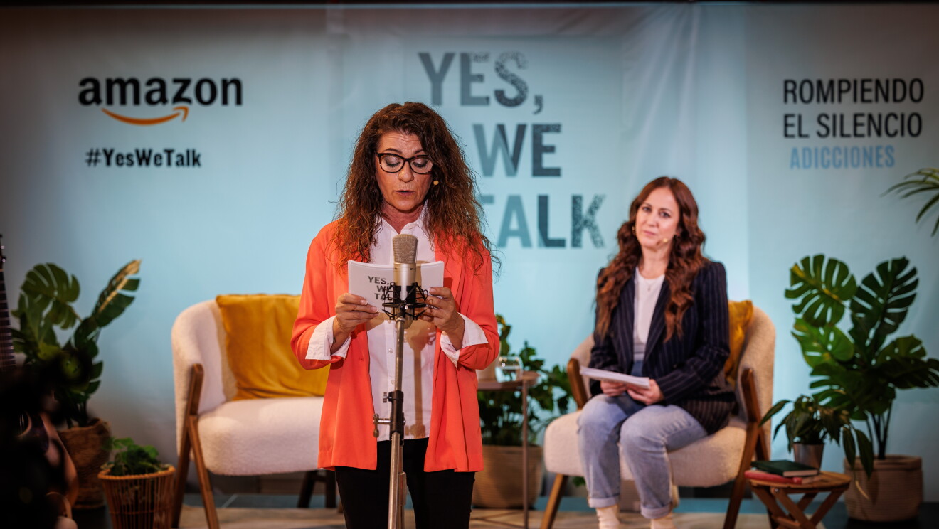 En un escenario creado para la ocasión, de fondo hay un cartel con el logo de Amazon y el Yes, we talk, que es el lema de la campaña. En el escenario, tres plantes con sus respectivas macetas, dos mesas y dos sillas y en una está sentada Mai Meneses. Mai Menses va con unas botas blancas, unos jeans, una americana negra y debajo un jersey de punto blanco. Dolores está de pie delante del mico, agarrando unas fichas y hablando. Dolores va vestida con unos pantalones negros y una americana naranja con una camisa blanca. Lleva gafas de pasta.  