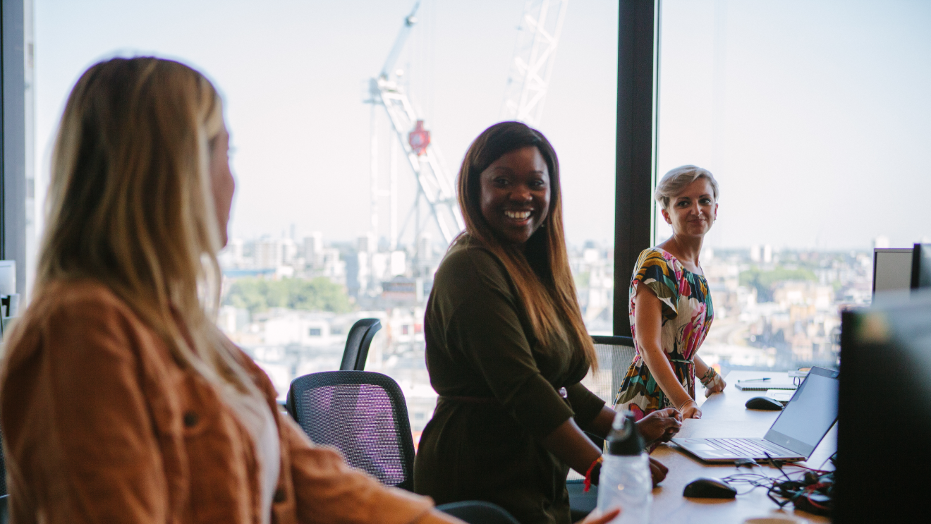 Three female employees stood at their desks, looking happy whilst working at Amazon head office 