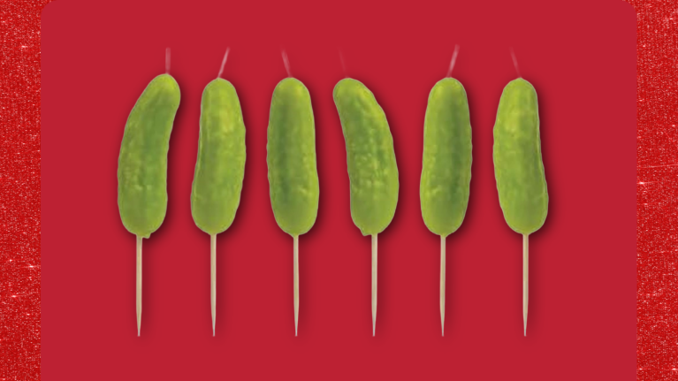 Six pickle candles on skewers against a bright red background