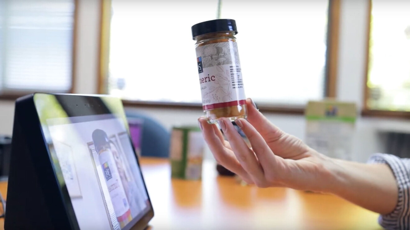 A hand holds a spice jar of Turmeric in front of an Echo Show to identify the product.