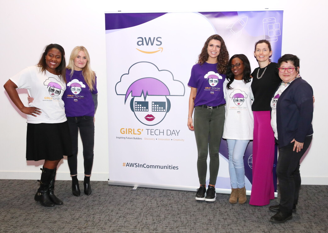 AWS InCommunities - Participating ladies and representatives of AWS standing in front of the AWSInCommunities Girls' Tech Day roll-up at an AWS InCommunity event