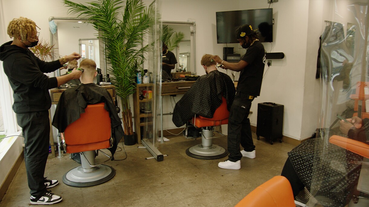 An image of two men cutting their clients' hair in a barber shop.