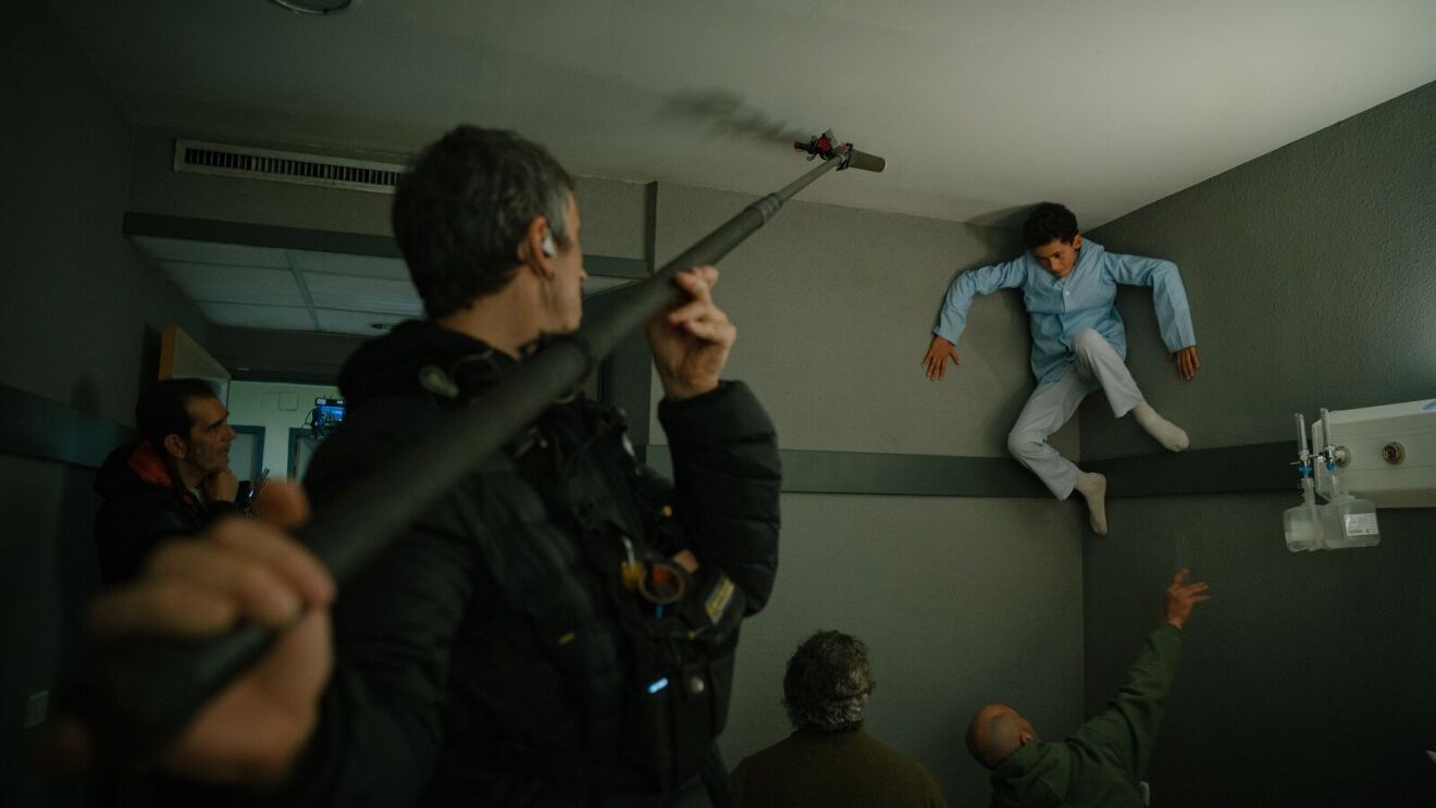 Man holding filming microphone toward a boy in the air on set