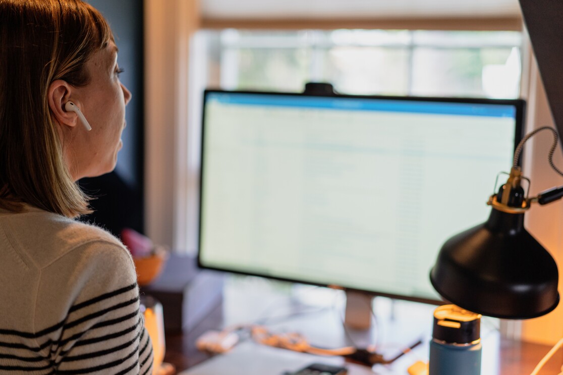 A woman wearing white wireless earphones works on a computer.