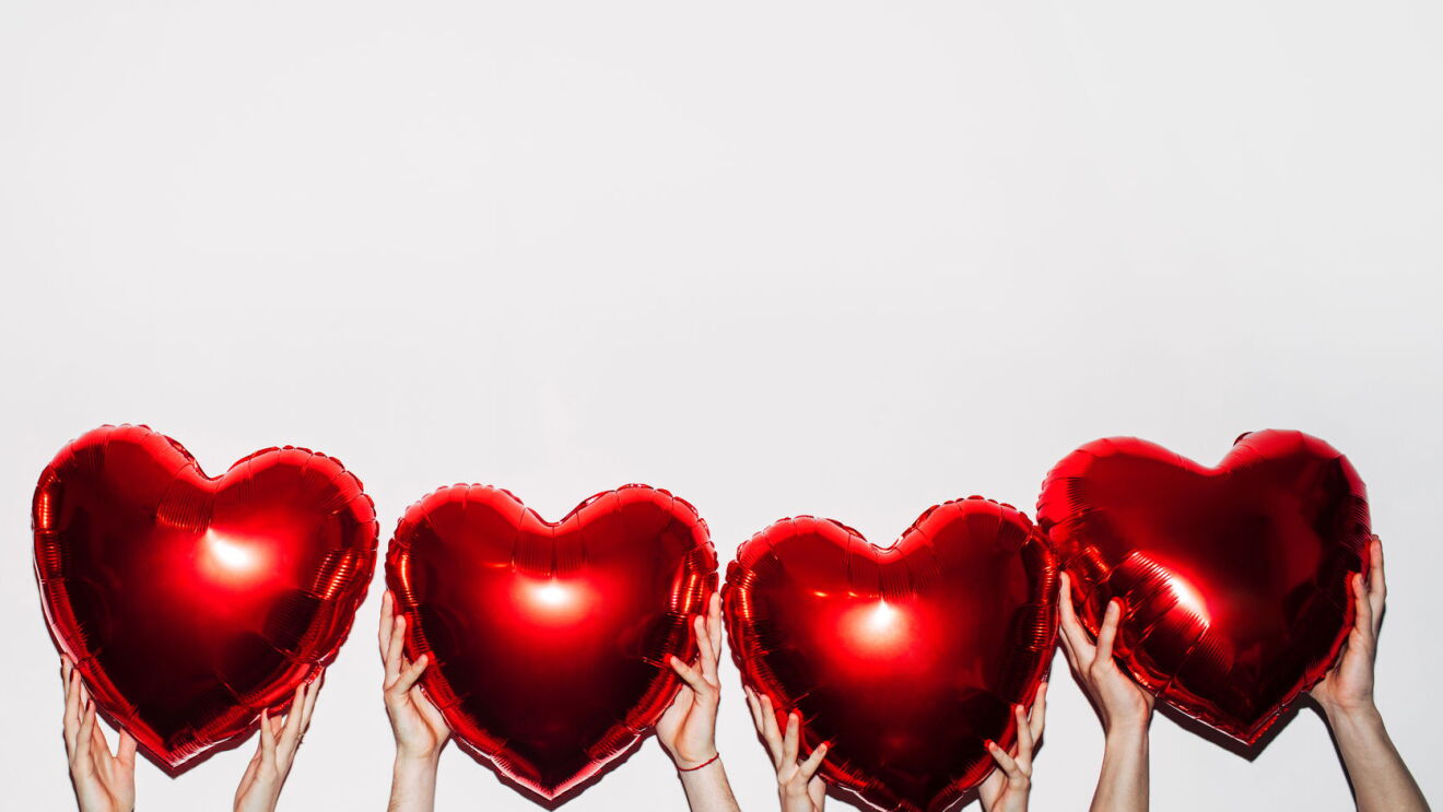 Four pairs of hands hold up heart-shaped balloons. 