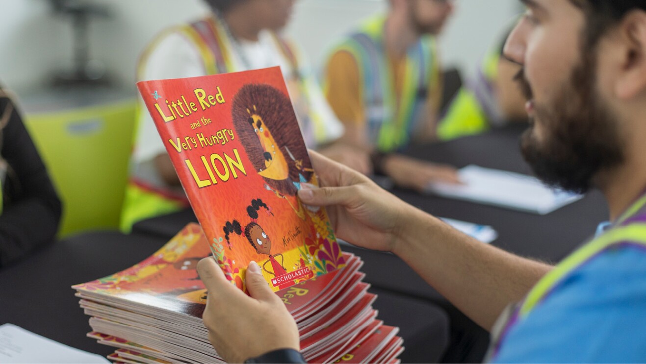 An image of a person holding a red book titled "Little Red and the Very Hungry Lion."