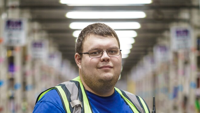 一名男子手持笔记本电脑。他戴着眼镜,穿着蓝色t恤和黄色安全背心。