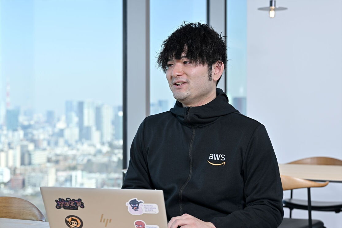 巻き毛と黒いジャケットを着た男性が微笑んでいる。杉山大夢さん。