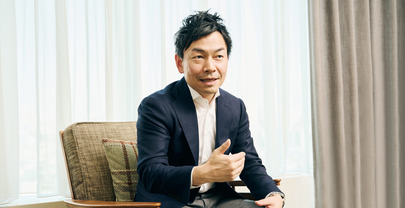椅子に座り話しているAmazonデバイス Fire TV 事業部 事業部長の西端明彦さん　紺色のジャケットを着ている