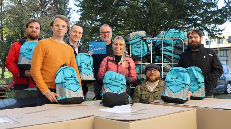 Mitarbeiter:innen des Amazon Verteilzentrums Klagenfurt im Rahmen der Aktion „Back-to-School“ mit blauen Rucksäcke für bedürftige und geflüchtete Kinder.