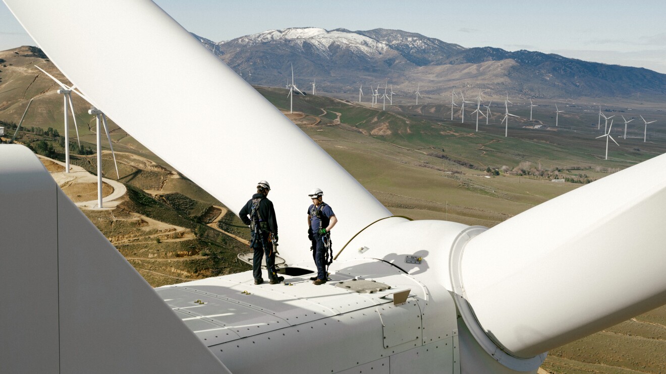 Technicians inspecting wind turbine blades overlooking landscape