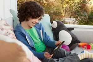 Child sitting on porch, smiling while viewing content on his tablet.