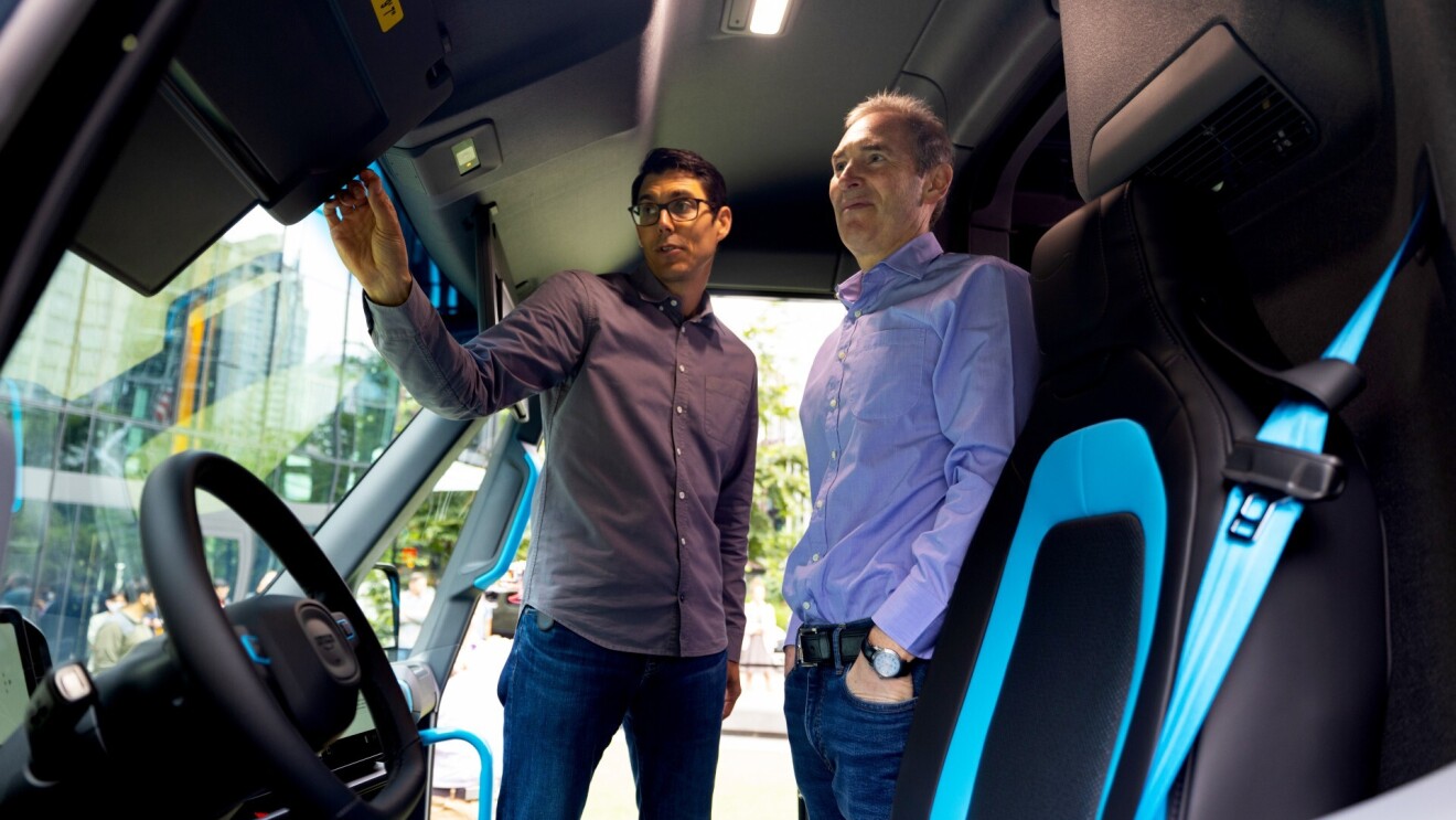 安迪雅西和RJ Scaringe站在Rivian亚马逊送货车辆停在亚马逊总部。Scaringe指向一个司机一侧的创新设计的一部分。