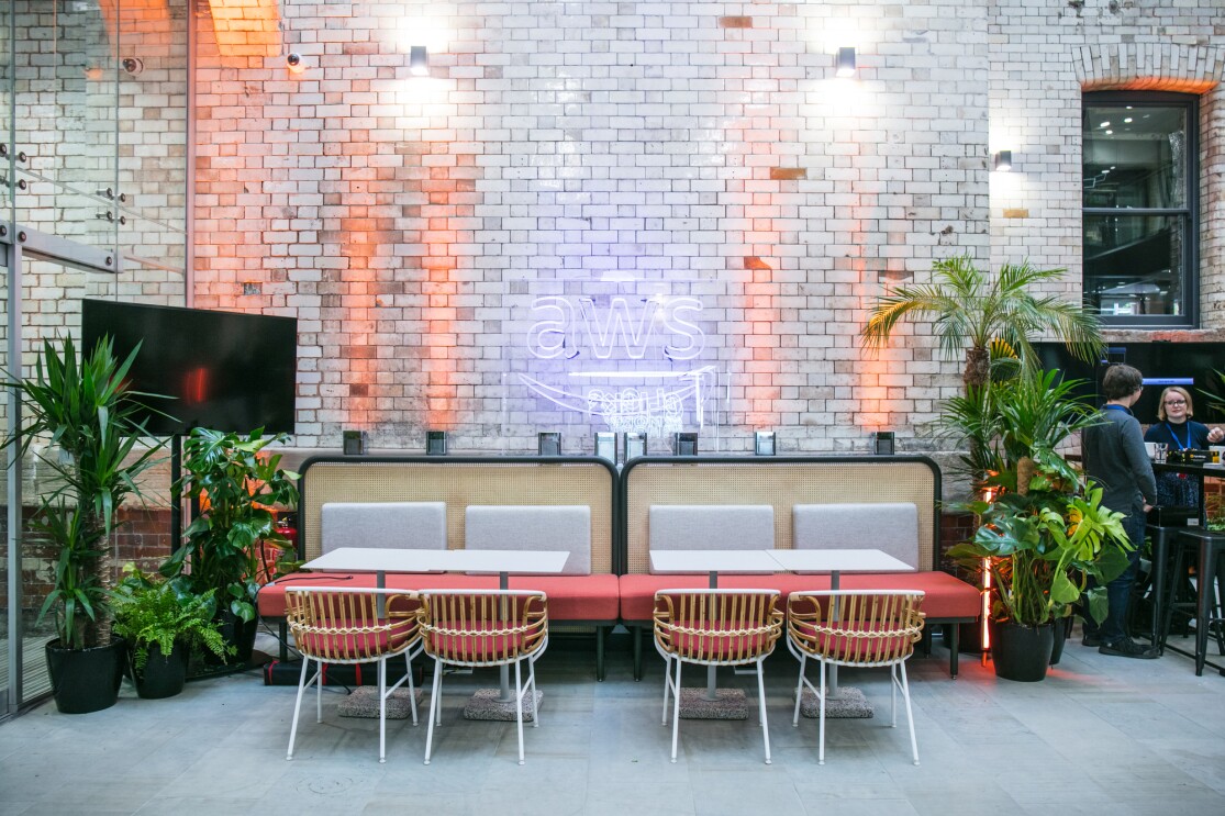 A modern office space with an AWS neon sign, a stylish seating area, plants, and brick walls