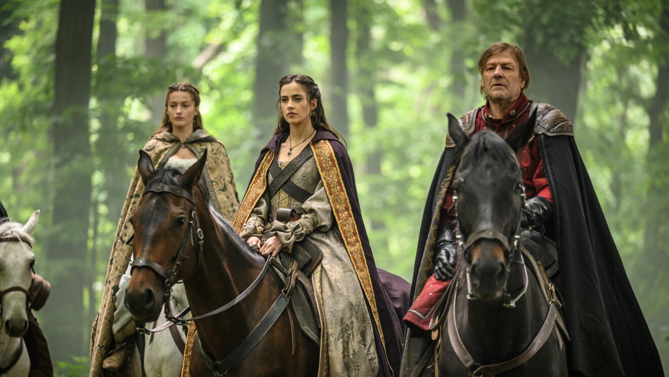 Three riders, including Robin Hood, on horseback in medieval attire traverse a misty forest