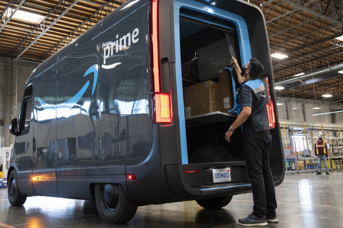 An Amazon delivery driver closes the back door of a Prime-branded Rivian van.