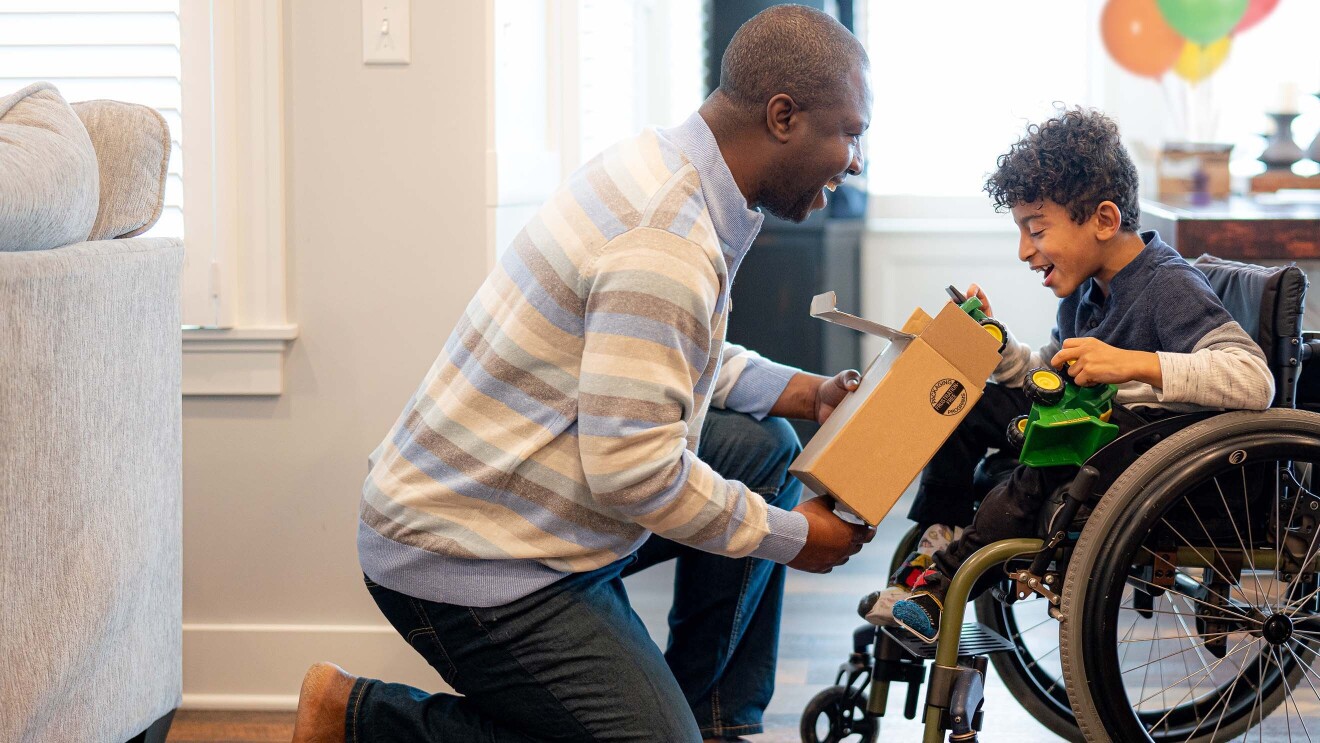 A child smiles as they open up a package that contains a green toy tractor.