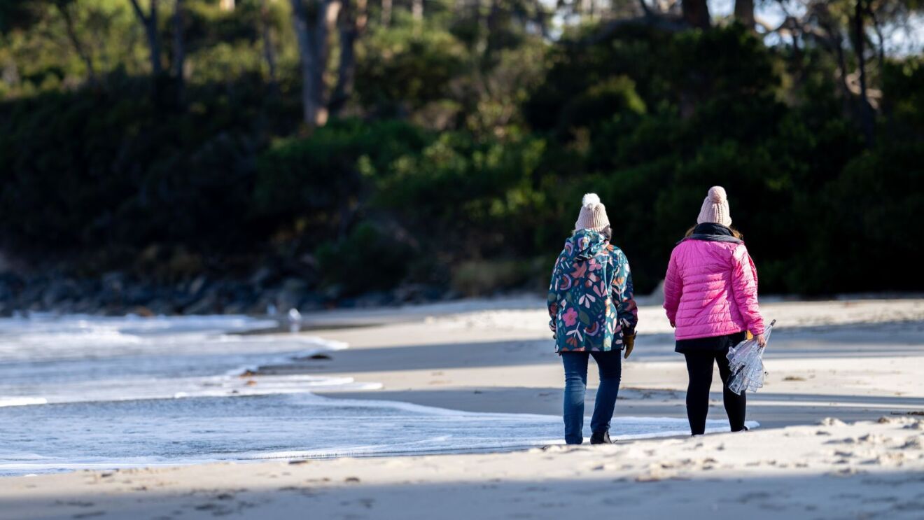 Two people walking along the beach in jackets and beanies 