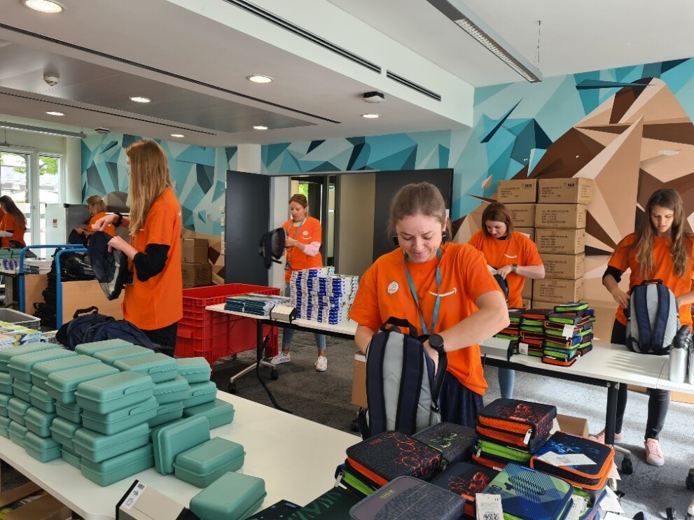 Amazon Mitarbeiter:innen an Packtischen, wie sie im Rahmen der Aktion "Back to school" Schulutensilien packen.