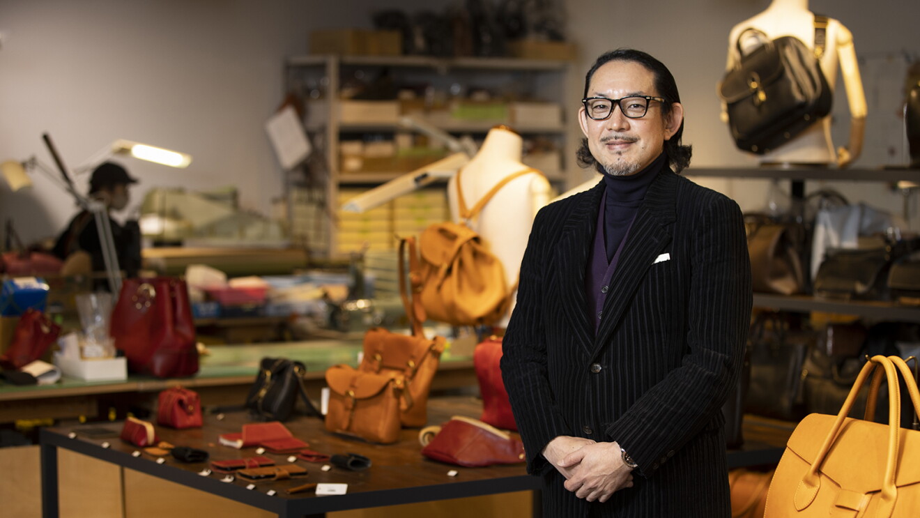 革製品が並べられた店内で商品棚の前に立つ、黒いベルベットのジャケットを着て、メガネをしているおしゃれな男性