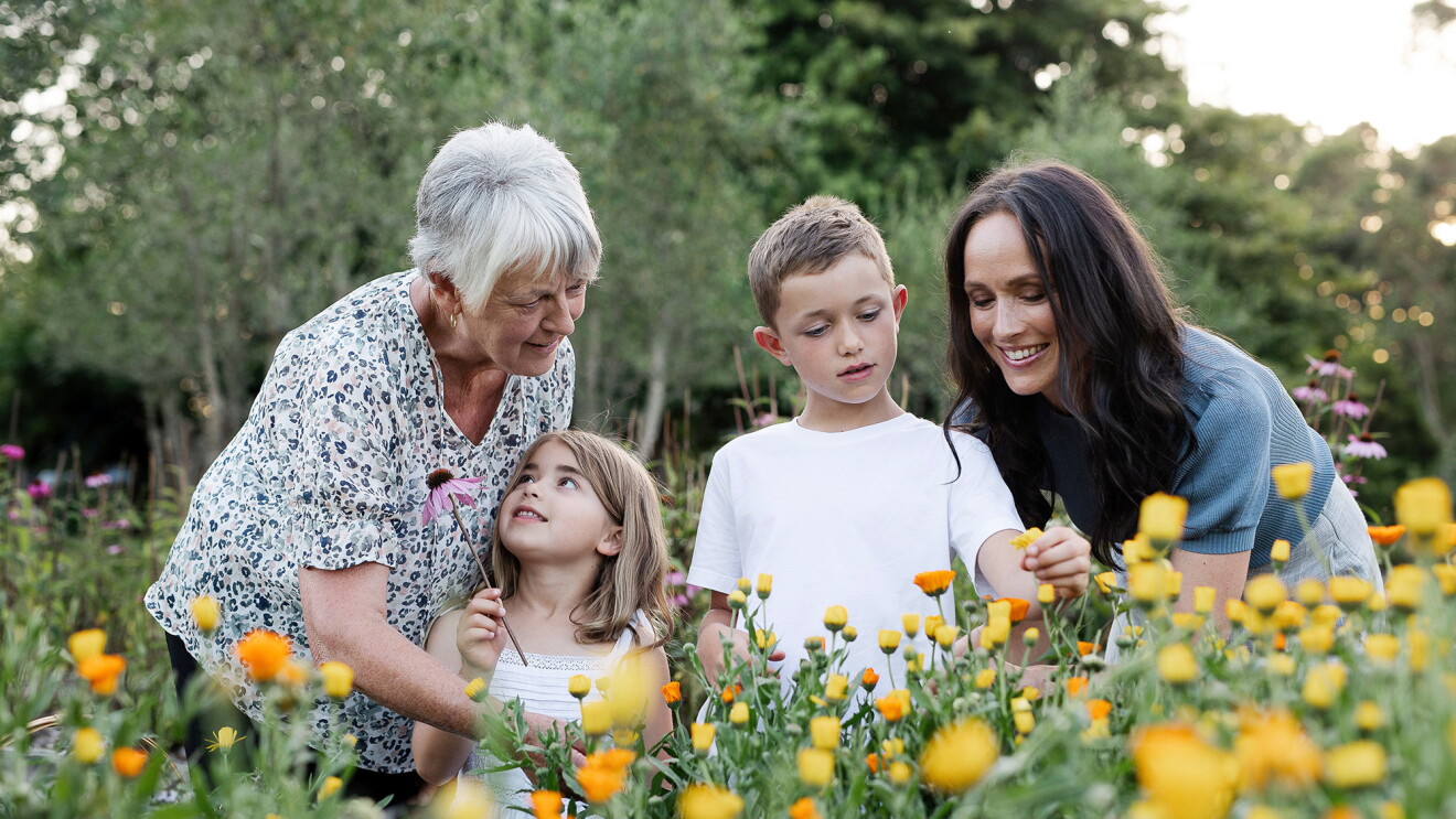 Three generations of a family stand in a floral garden and engage with eachother.