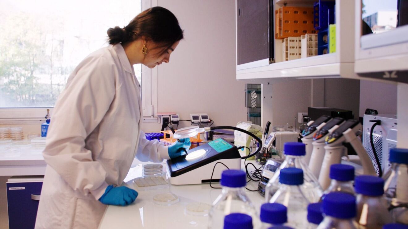 Scientist in lab coat working at bench with equipment and bottles