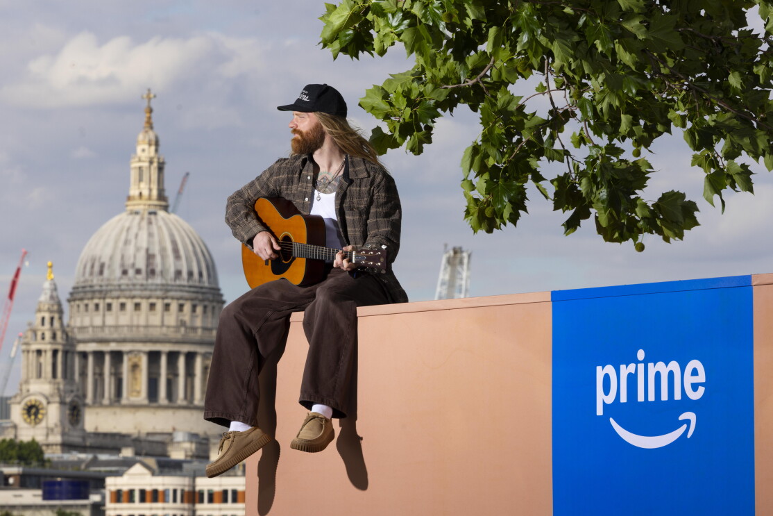 Sam Ryder sitting on a giant Amazon box at Southbank playing the guitar. 