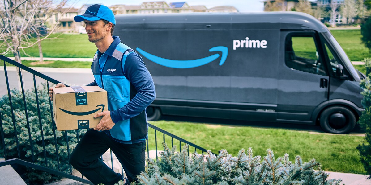 Amazon Prime delivery driver walks up the steps to deliver a package with his Prime delivery van in the background.