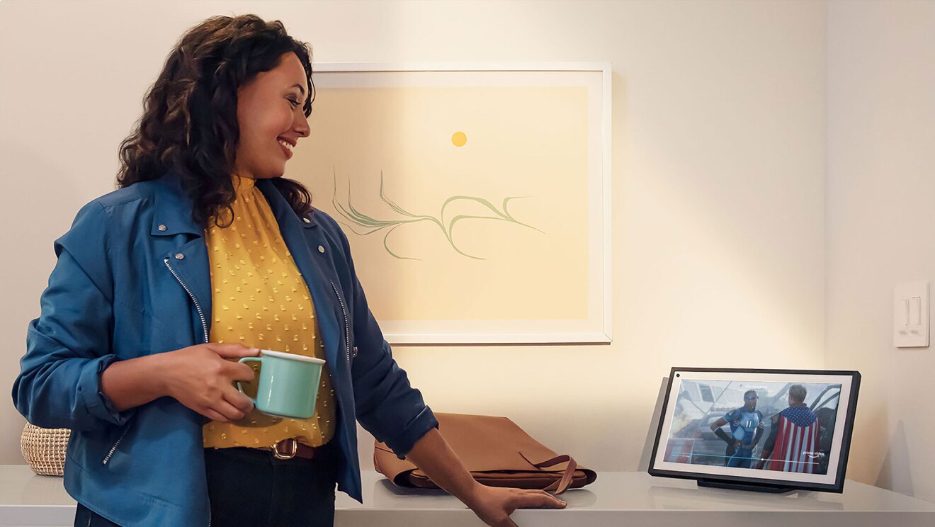 A woman holding a mug looking at her Echo device.