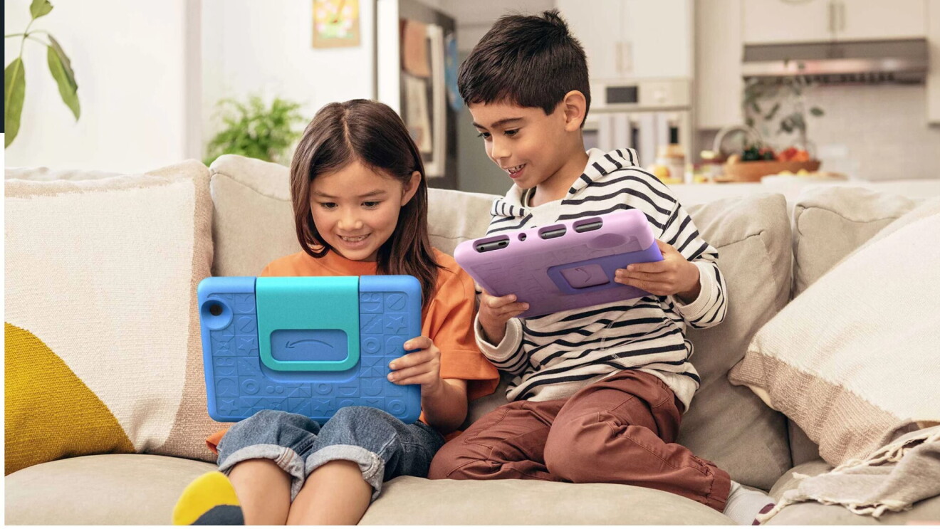 Dos niños en el sofá jugando con su tablet respectiva.