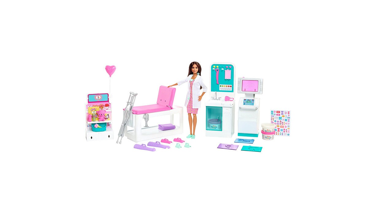 an image of a Barbie doll in a white doctor's coat. She is standing among a setup of a clinic with different medical devices and equipment.