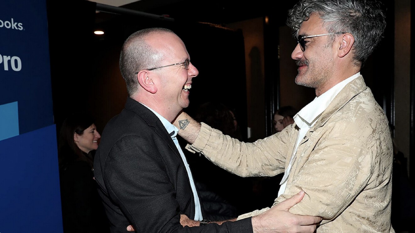 A photo of Col Needham, founder and CEO of IMBD, Embracing Taika Waititi.