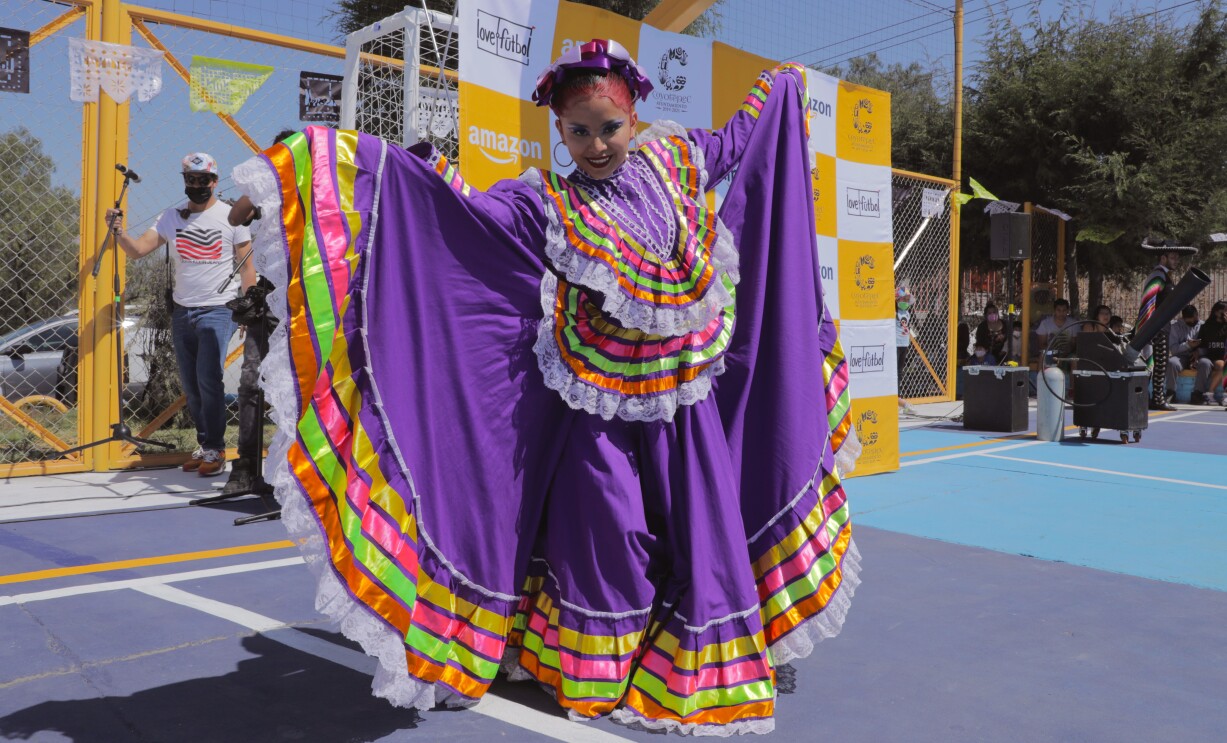 En una cancha de fútbol una mujer con el traje tradicional de México. 