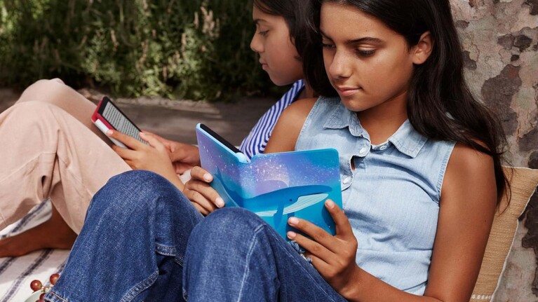 Two young girls reading books together outdoors