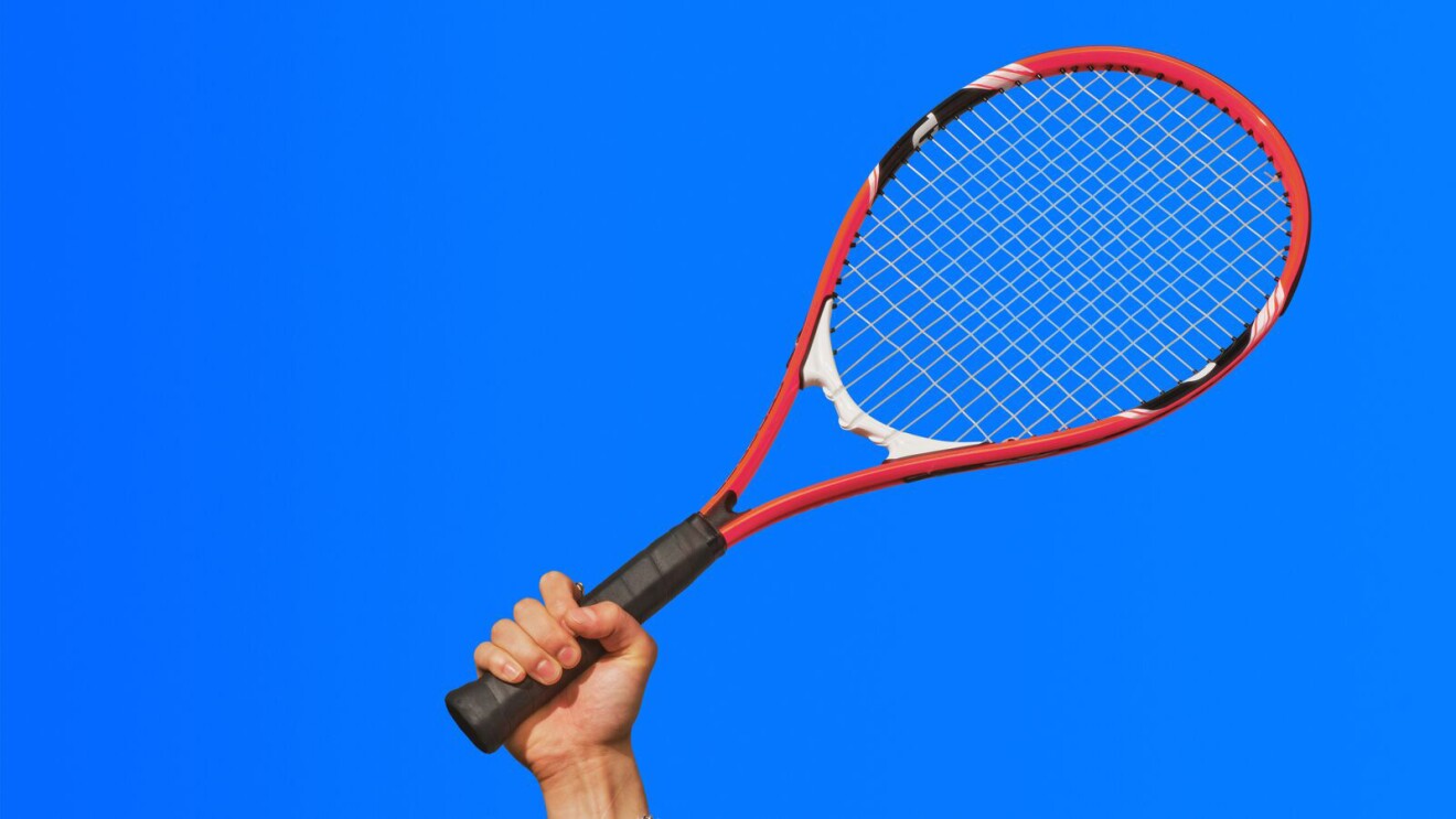 Hand gripping red tennis racket against bright blue background